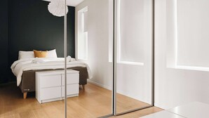 Ein Schlafzimmer mit einem Bett, einer weißen Kommode, einem Spiegel und einem Fenster.