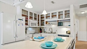 Una cocina moderna con armarios blancos, una isla central con platos azules y un refrigerador blanco.