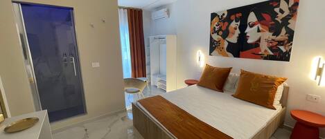 A modern hotel room with a large bed, a desk, a chair, and a wardrobe.