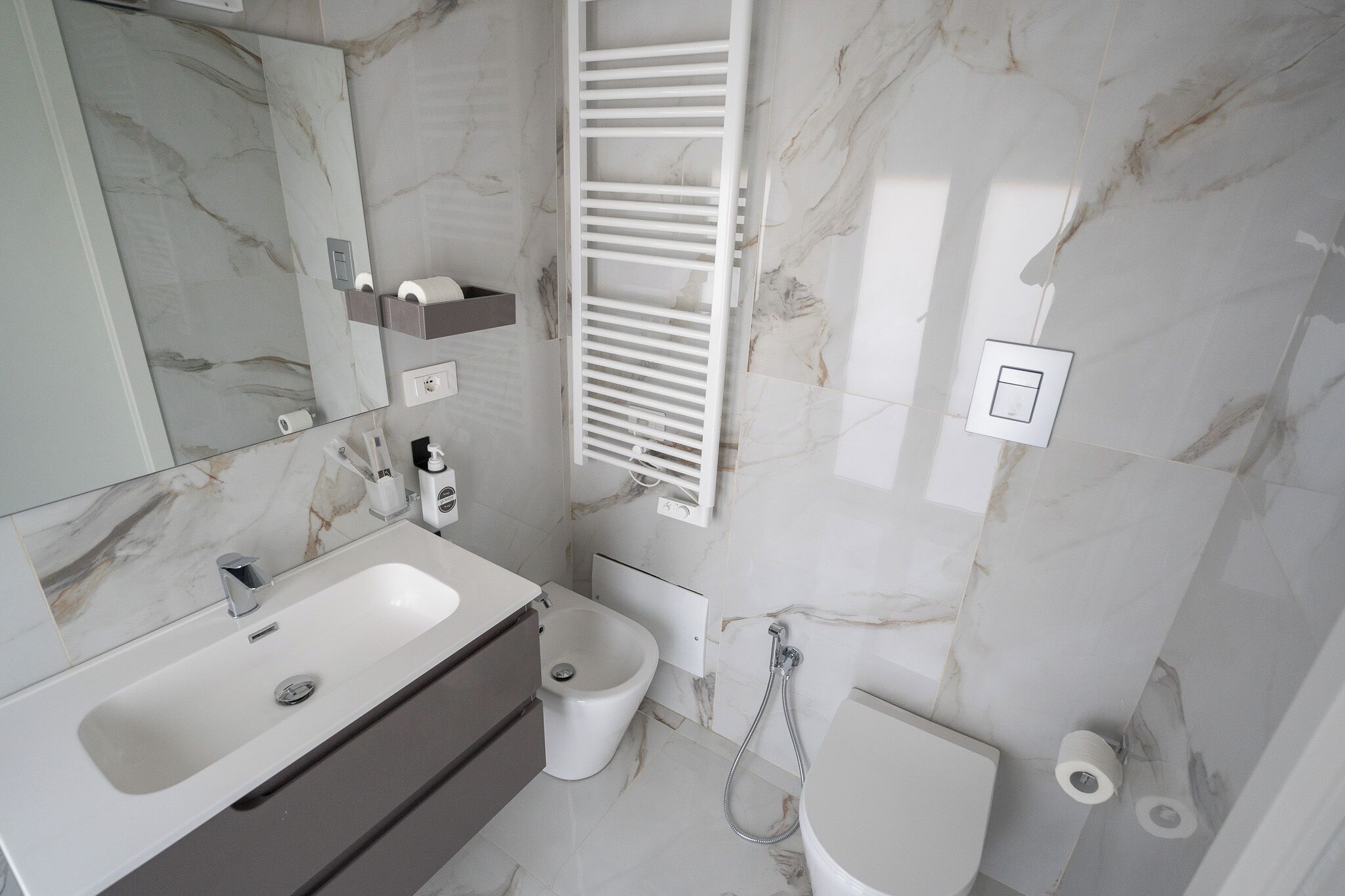 A modern bathroom with a marble backsplash, a white sink, a bidet, and a toilet.
