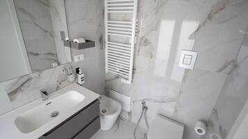 A modern bathroom with a marble backsplash, a white sink, a bidet, and a toilet.