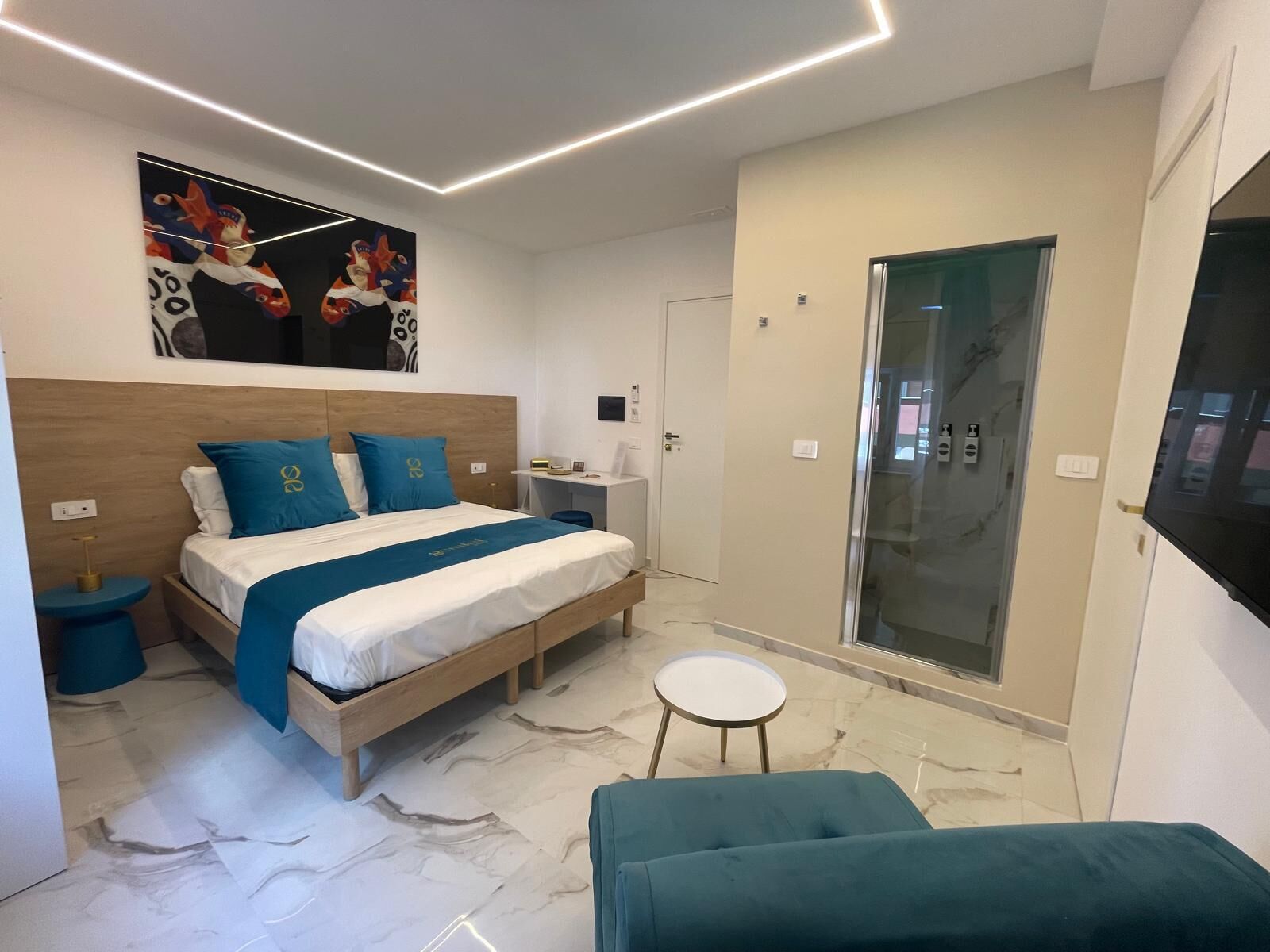 A modern bedroom with a bed, bedside tables, a desk, and a glass shower enclosure.