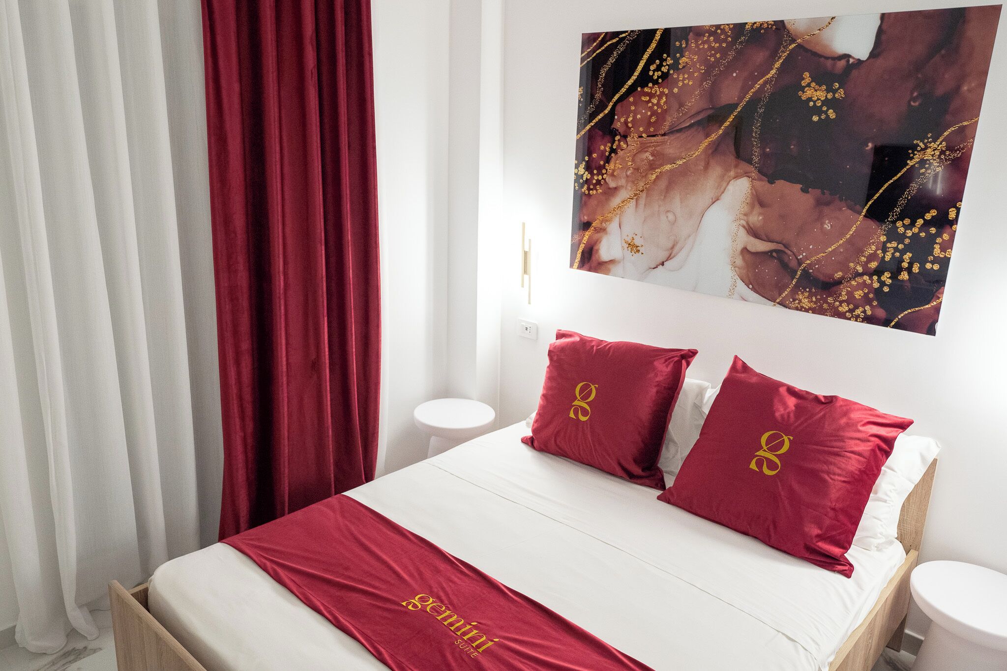 A hotel room with a bed, red curtains, a white wall, and a painting.