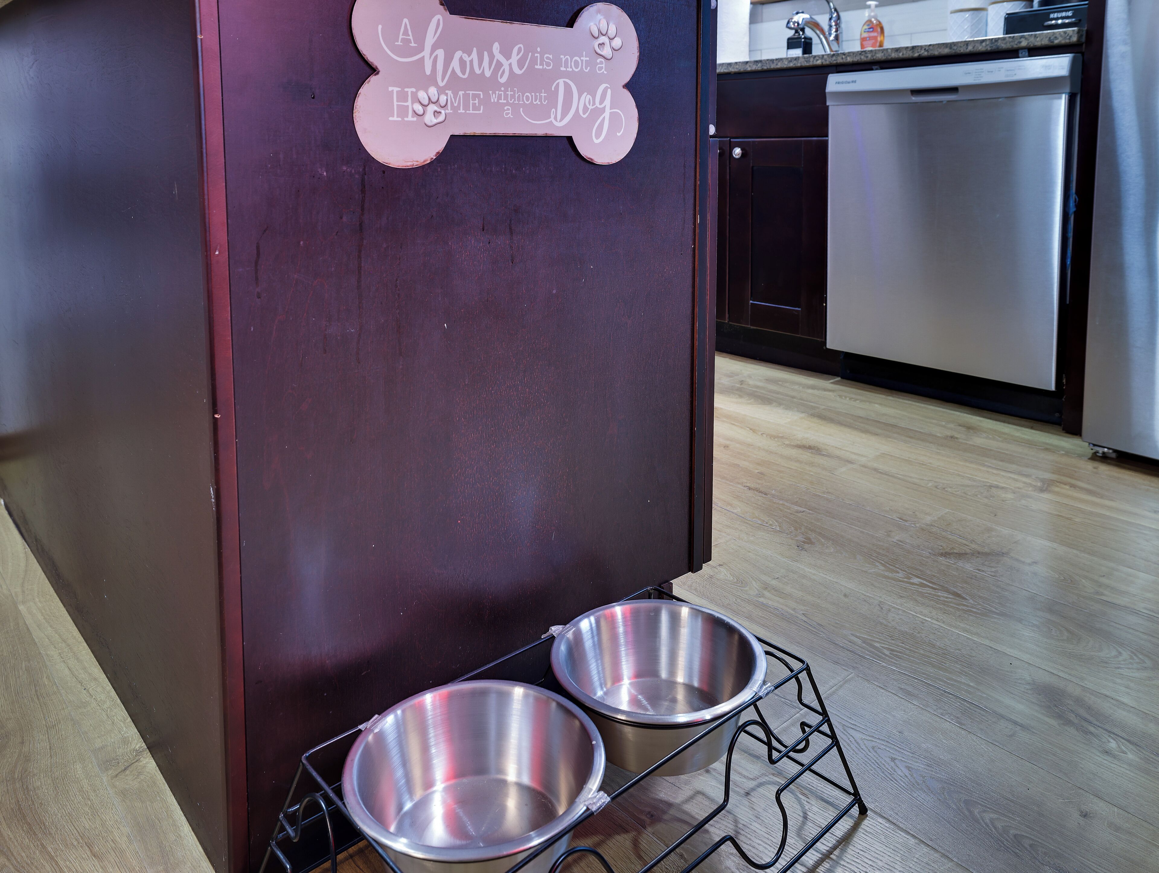 A kitchen with a dark wooden cabinet, a stainless steel sink, and two metal dog bowls on a wire rack.