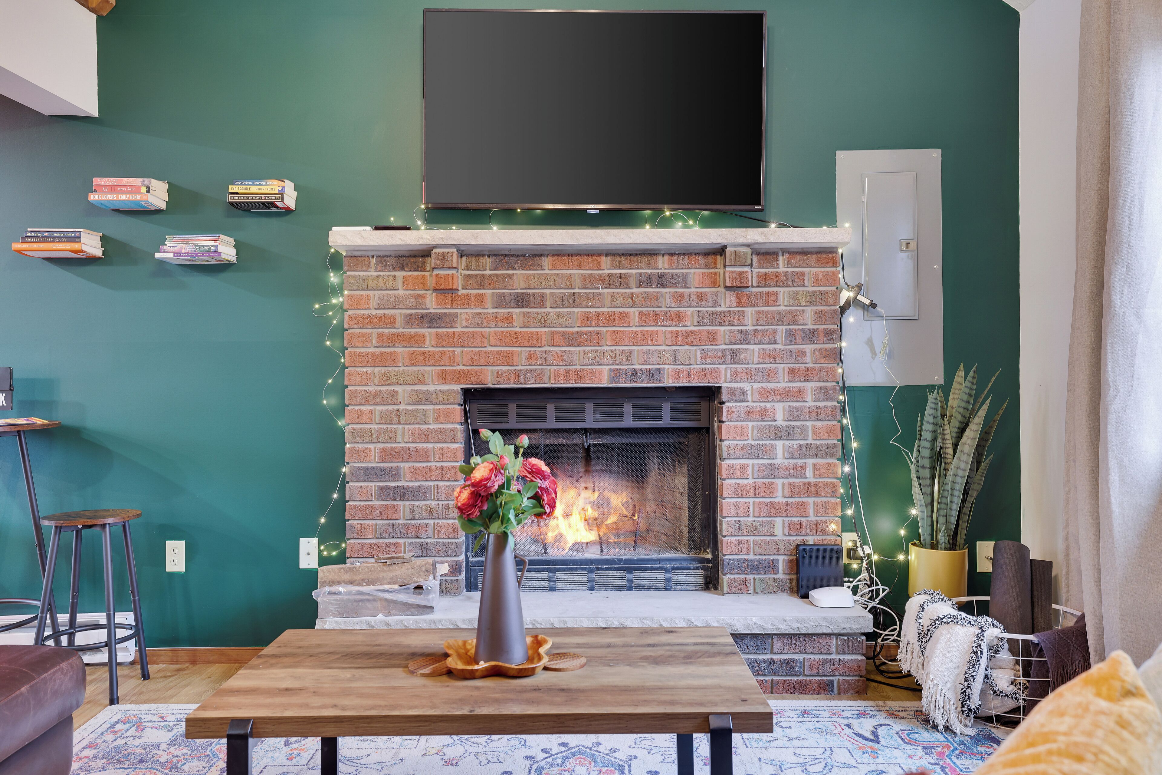 A cozy living room with a brick fireplace, a flat-screen TV mounted above it, and a table with a vase of flowers.