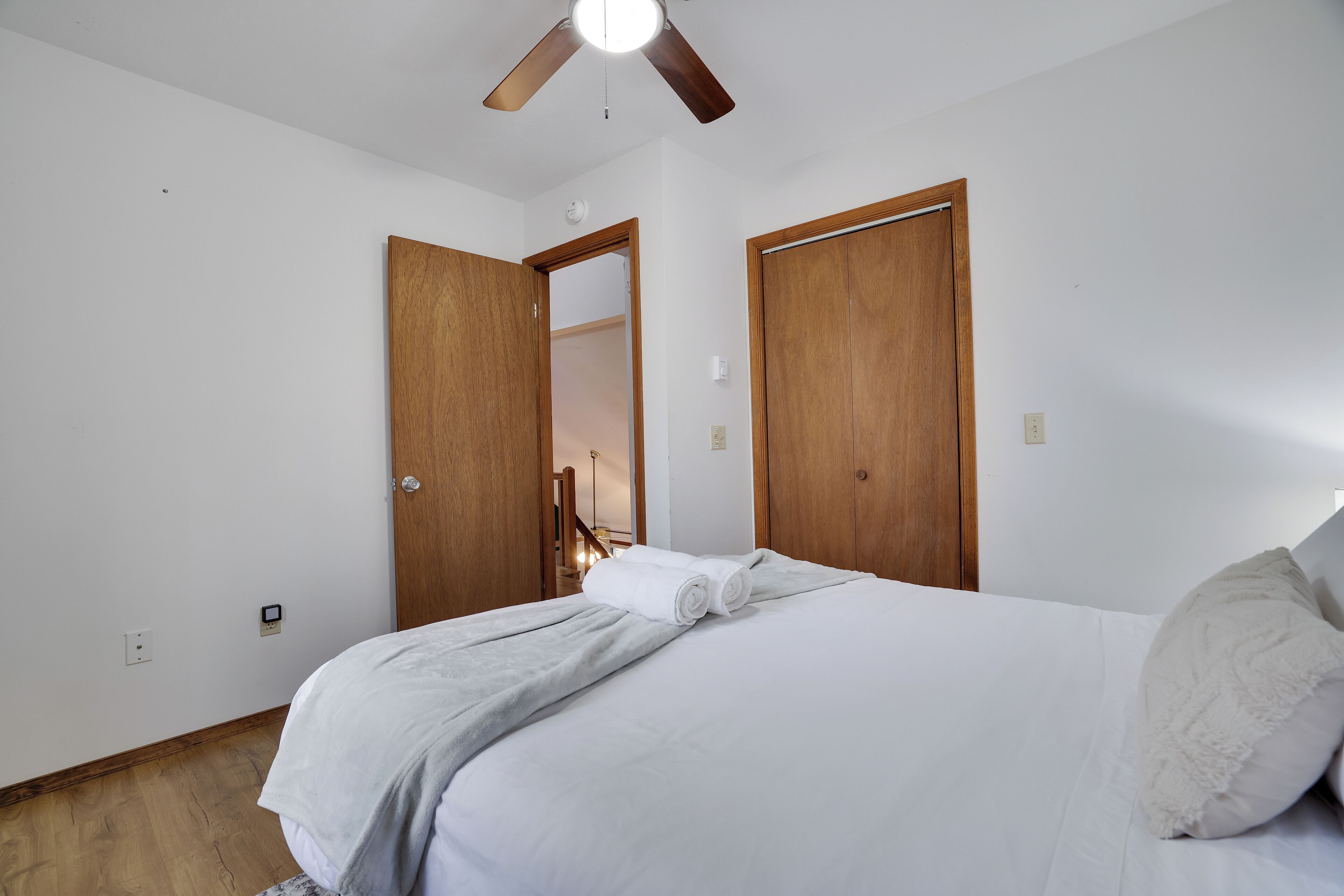 A bedroom with a bed, white linens, a ceiling fan, and wooden doors.