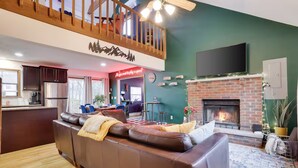 Un salón amplio con un sofá de cuero marrón, una chimenea y un televisor montado en la pared.