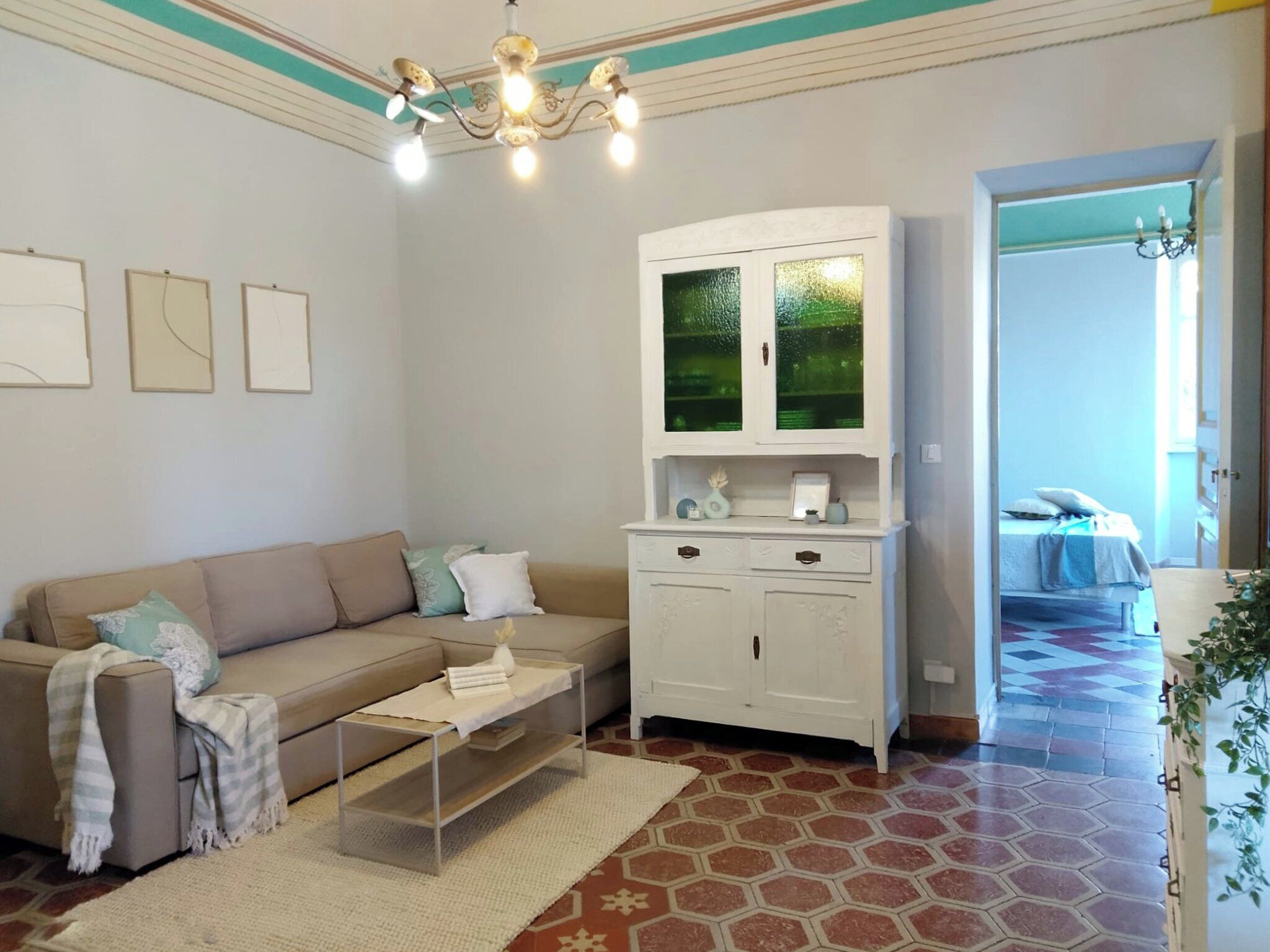 A living room with a beige sofa, a white cabinet with glass doors, a coffee table, and a patterned floor.