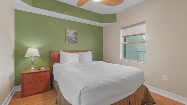 Un dormitorio ordenado con cama, mesita de noche, lámpara y ventana.