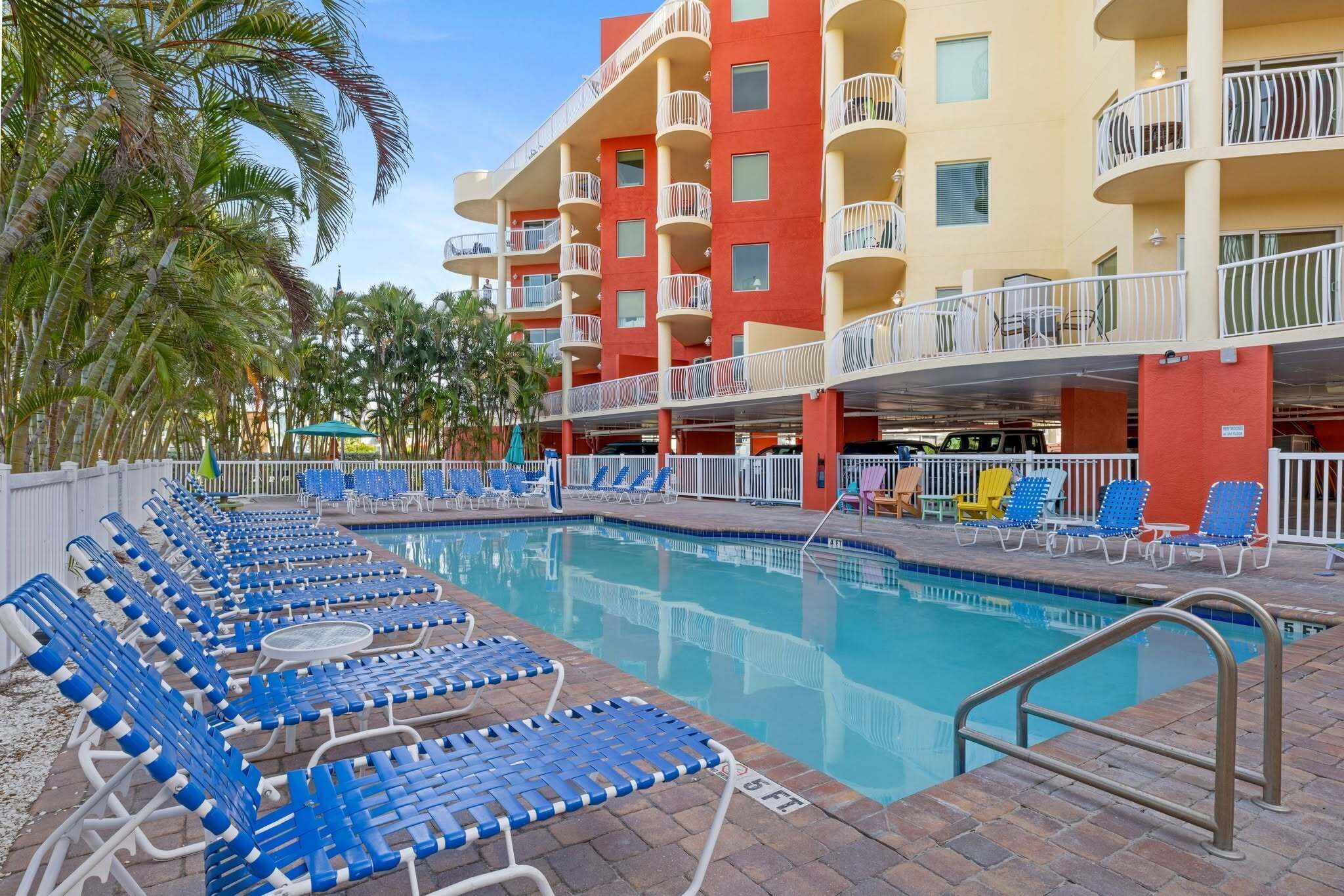 A pool area with blue lounge chairs and a building with balconies.