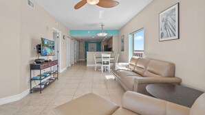 A spacious living area with a beige sofa, a TV mounted on the wall, and a dining table with chairs. - Upscale Comfort with and Affordable Price 🏝 Beach Access across the street (Treasure Island)