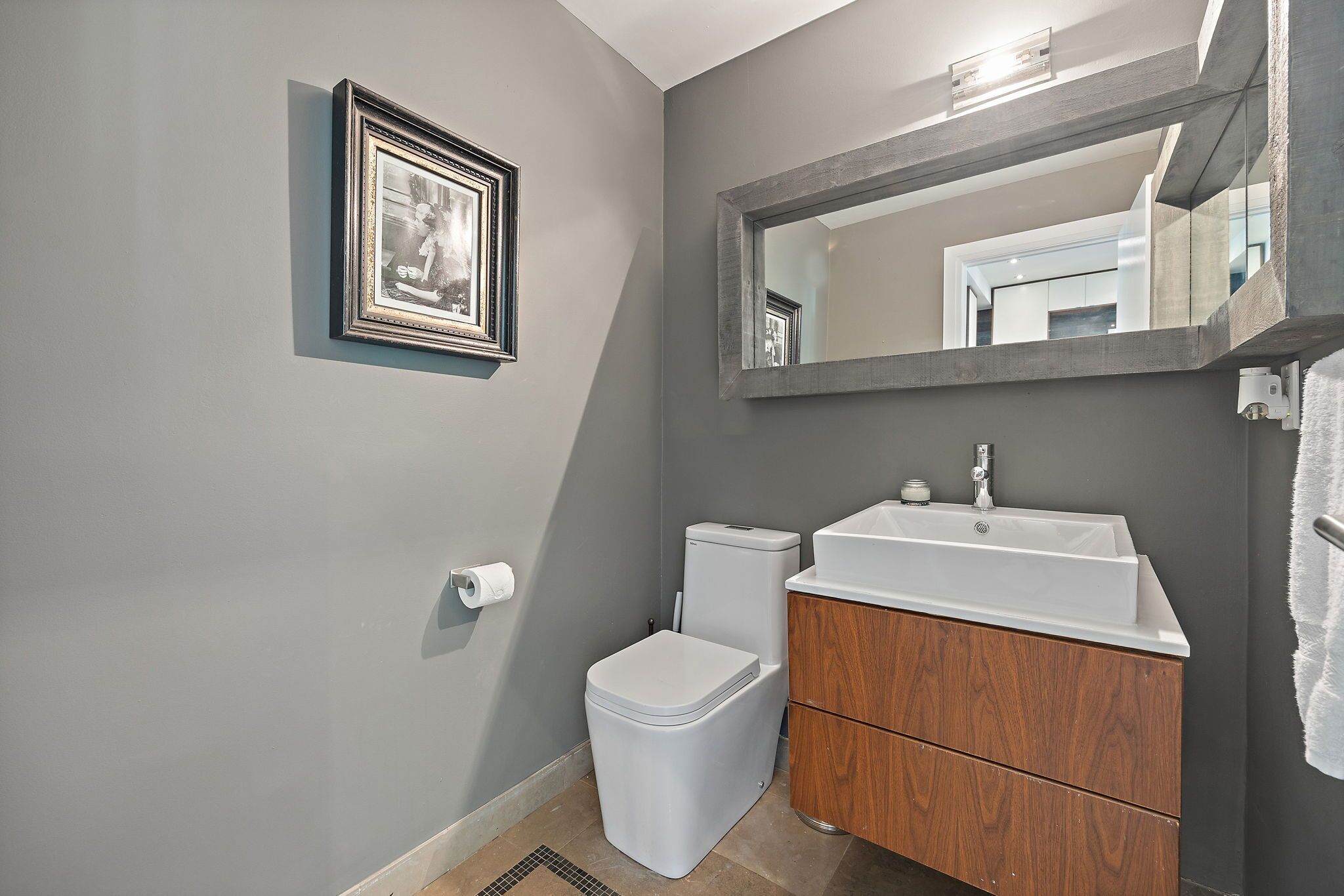 A bathroom with a toilet, sink, vanity, and a framed picture on the wall.