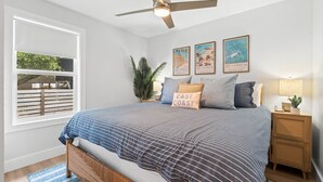 Un dormitorio con una cama, ventilador de techo, mesita de noche, lámpara y decoración en la pared.