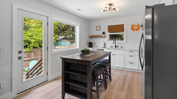 Una cocina moderna con gabinetes blancos, una isla central con taburetes, horno empotrado y refrigerador.