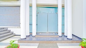 L’entrée d’un immeuble est agrémentée d’un escalier menant à une porte en verre, flanquée de colonnes blanches.