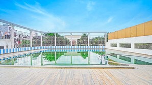 Une piscine dotée d’une terrasse en bois, entourée d’un bâtiment blanc agrémenté de touches de bleu et d’une clôture.
