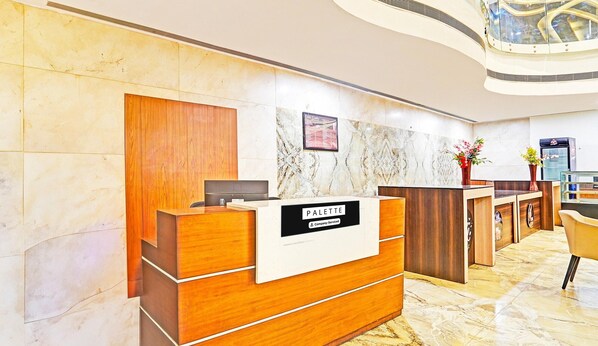 A reception desk with a sign reading "PALETTE Company-Serviced" in a modern lobby with marble flooring and wooden paneling.