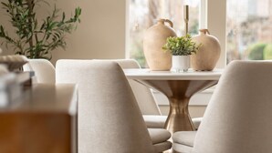 Un comedor con una mesa y sillas, una planta en maceta y jarrones decorativos.