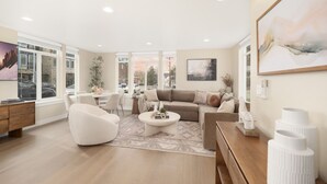 Una sala moderna con sofá, mesa de centro y sillones. Hay un comedor con mesa y sillas. La habitación tiene ventanas grandes y vistas al exterior.