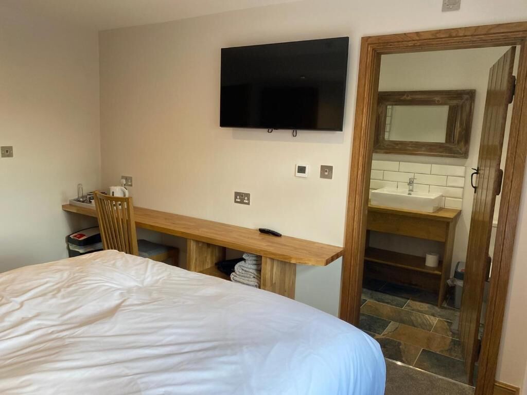Una camera da letto con un letto, una scrivania, una televisione e un bagno con lavandino e specchio.