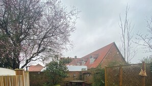A backyard with a wooden fence, a grassy lawn, a brick house with a red roof, and a tree with pink blossoms. - Maypole Farm Guest House (Selby)