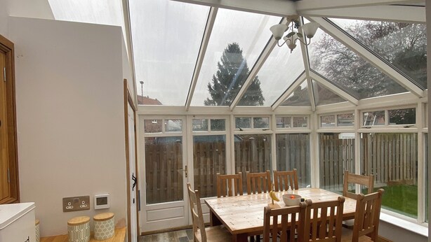 A conservatory with a dining table and chairs, a bread box, and a washing machine. - Maypole Farm Guest House (Selby)