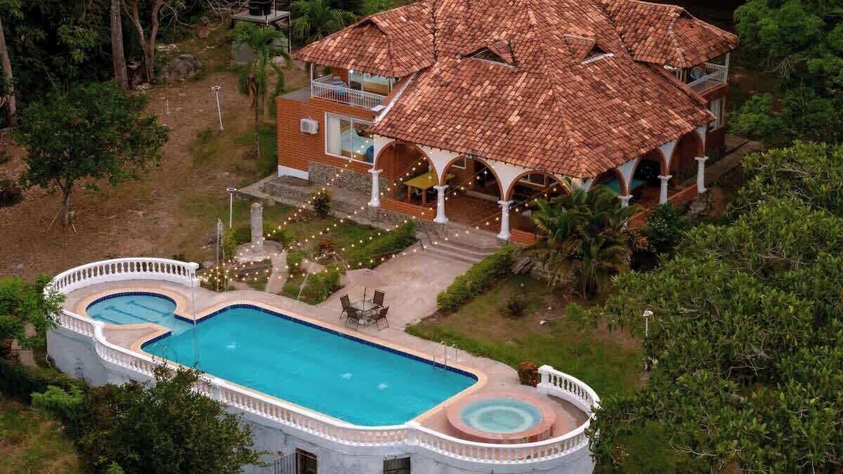 Una casa grande con piscina, rodeada de vegetación.