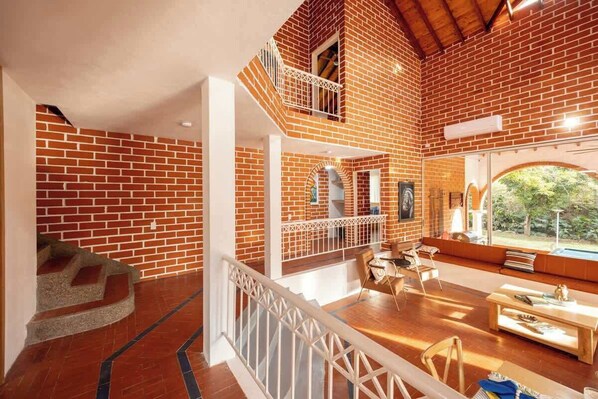 A spacious loft with exposed brick walls, a wooden staircase, a balcony with a railing, and a dining area with a table and chairs.