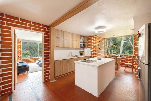 A modern kitchen with a brick wall, wooden cabinets, a central island, and a view through large windows.