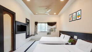 A hotel room with two beds, a ceiling fan, a TV, and artwork on the wall. - Elegant Escape in Palette Bhimpore Daman (Daman)