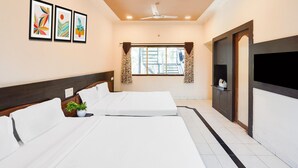 A hotel room with two beds, a ceiling fan, a window with curtains, and framed artwork on the wall. - Elegant Escape in Palette Bhimpore Daman (Daman)