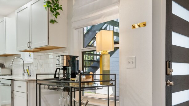 Eine moderne Küche mit weißen Schränken, einem schwarzen Metalltisch und einem Fenster mit Blick auf ein Haus.