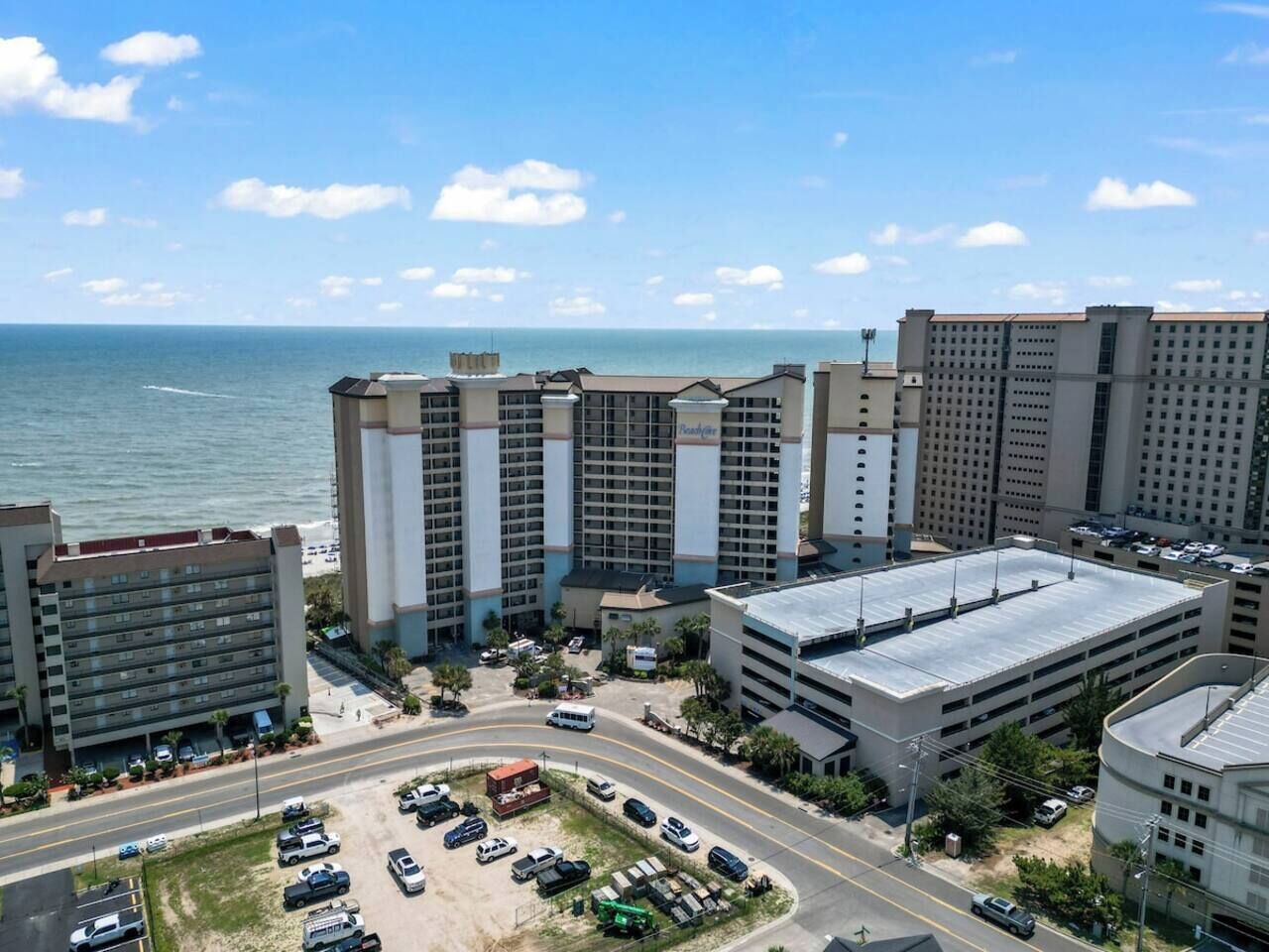 A high-rise hotel with multiple floors, a parking lot, and a view of the ocean.