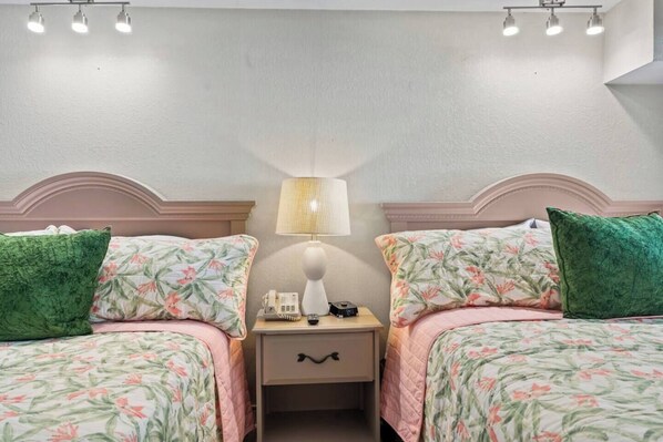 Una habitación de hotel con dos camas, una mesita de noche con lámpara y una lámpara de pared.