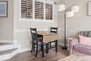 A dining area with a wooden table, two chairs, a floor lamp, and a sofa.