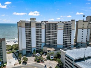 A beachfront hotel with multiple high-rise buildings, a parking area, and a beach in the background. - Beachfront Haven | Ocean Views & Pool | Sleeps 4 (North Myrtle Beach)
