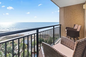 Un balcón con vista al océano, muebles de mimbre y barandilla.