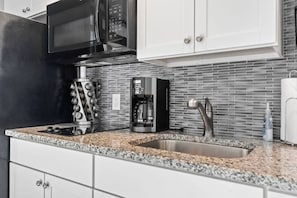 A kitchen with a microwave, coffee maker, and a stainless steel sink.