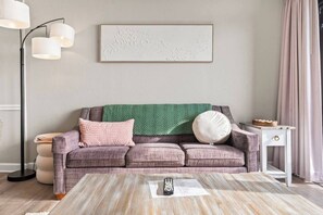 A living room with a sofa, a coffee table, a floor lamp, a side table, and a wall-mounted artwork. - Beachfront Haven | Ocean Views & Pool | Sleeps 4 (North Myrtle Beach)