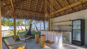 Un espacio de descanso frente a la playa con mobiliario de madera, una hamaca y una cocina moderna.