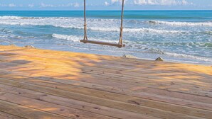 Una terraza de madera con un columpio frente al océano.