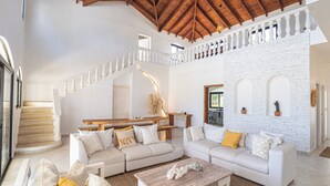 Un amplio salón con techo alto, una escalera y una pared de ladrillo blanco.