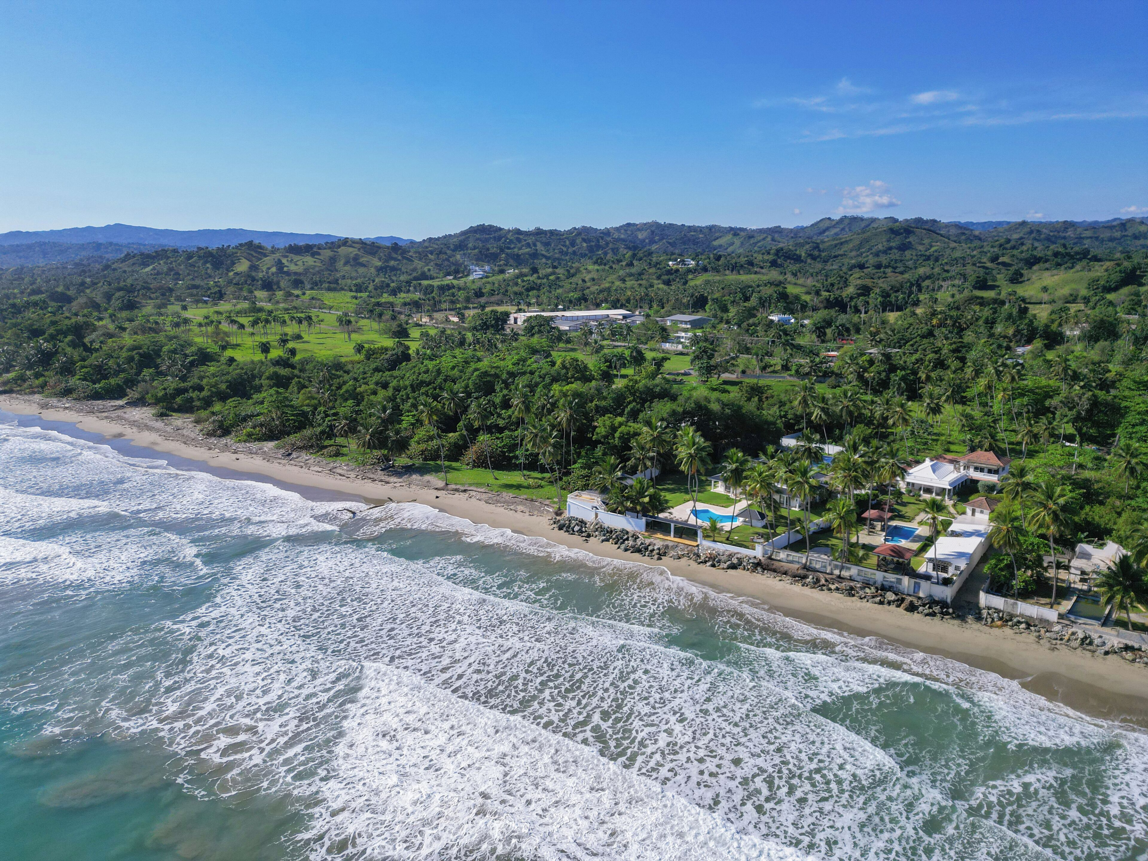 A coastal property with a beach, ocean waves, and a lush green landscape.