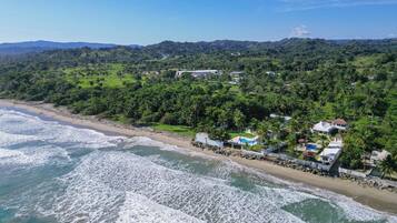 A coastal property with a beach, ocean waves, and a lush green landscape.