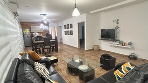 A modern living room with a black leather sofa, a glass coffee table, and a dining area with a table and chairs. - IDEAL HOUSE TO REST, SWIMMING POOL, BBQ, WIFI, FULL AIRE (Sabanilla)