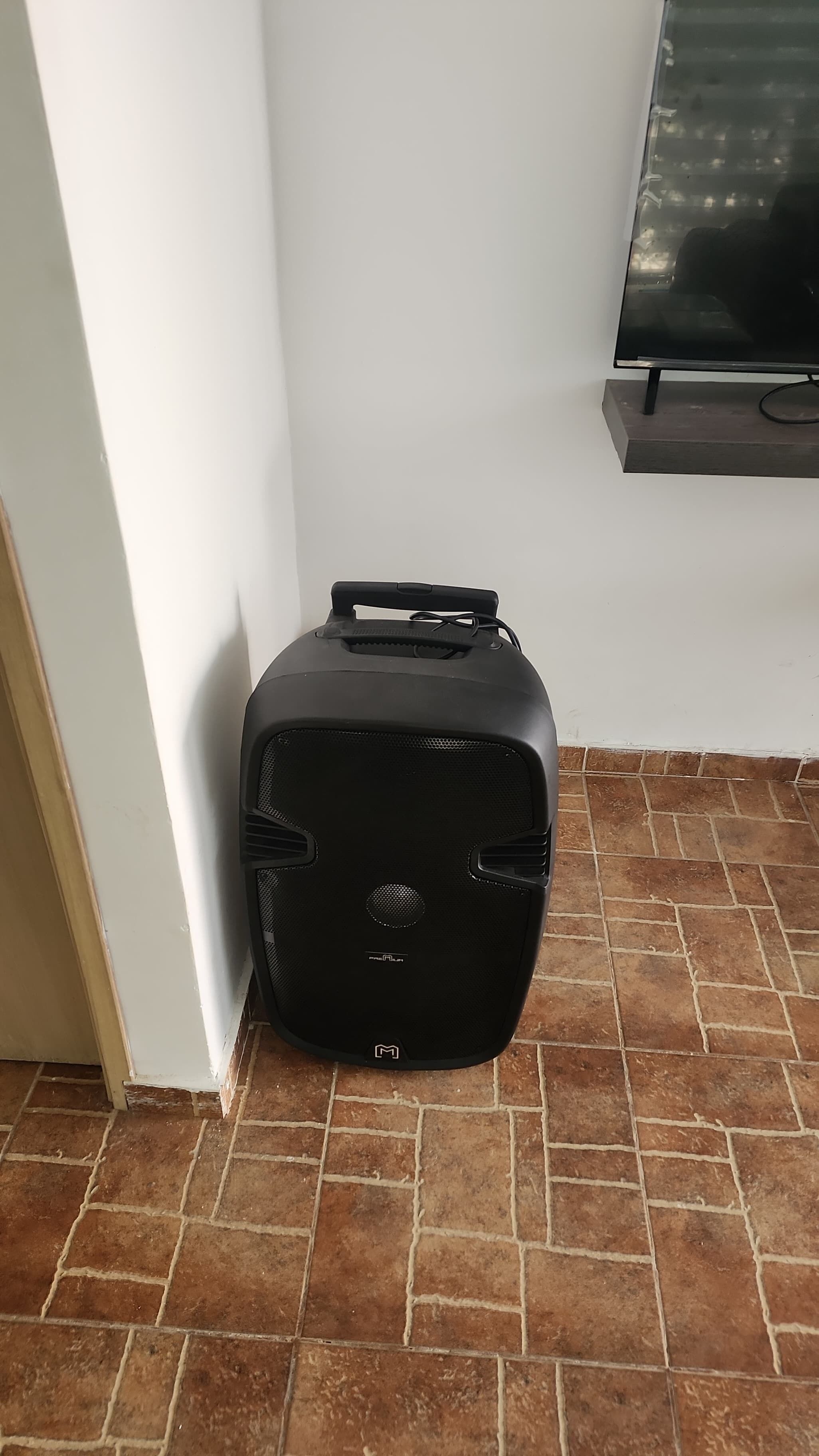Una maleta negra sobre un suelo de baldosas, junto a una pared blanca y un televisor de pantalla plana montado en la pared.