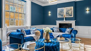 Habitació amb un sofà blau, una llar de foc i un finestral gran amb detalls blancs.