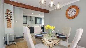 A dining area with a glass table surrounded by four chairs, a vase with yellow flowers, and a wooden wall clock.