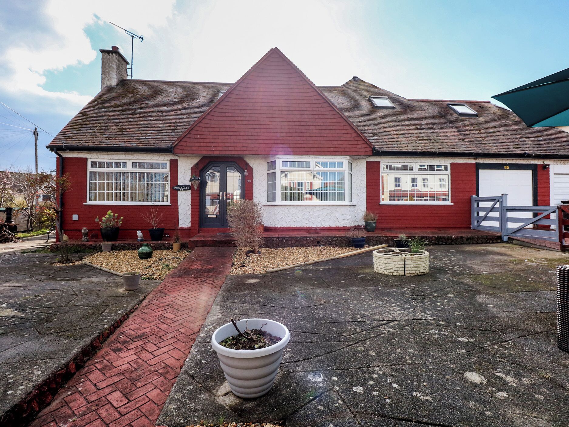 A red brick house with a tiled roof, a front door, and a small garden with potted plants.