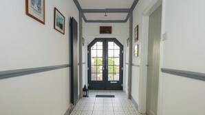 A hallway with patterned floor tiles, a black door with glass panels, and framed pictures on the walls.